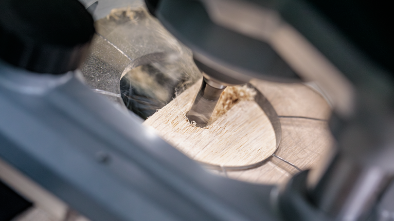 Alat putar yang mengebor lubang presisi pada papan kayu.