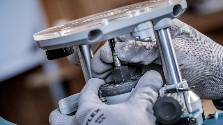 Orang yang mengenakan peralatan keselamatan menyesuaikan alat router menggunakan tangan bersarung tangan.