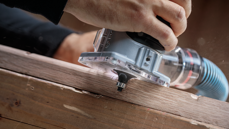 Seseorang menggunakan router genggam untuk membentuk tepi papan kayu.