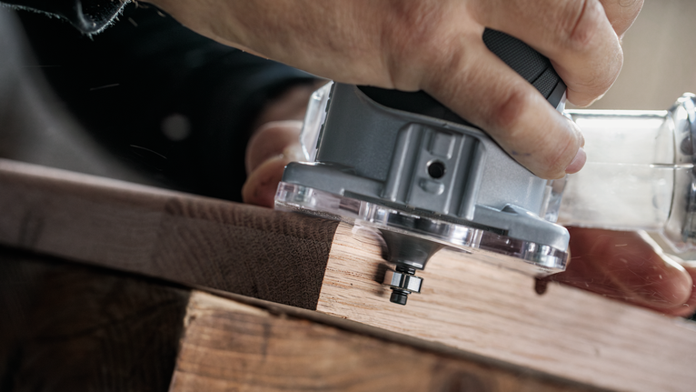 Seseorang sedang mengarahkan pemangkas listrik di sepanjang tepi papan kayu.