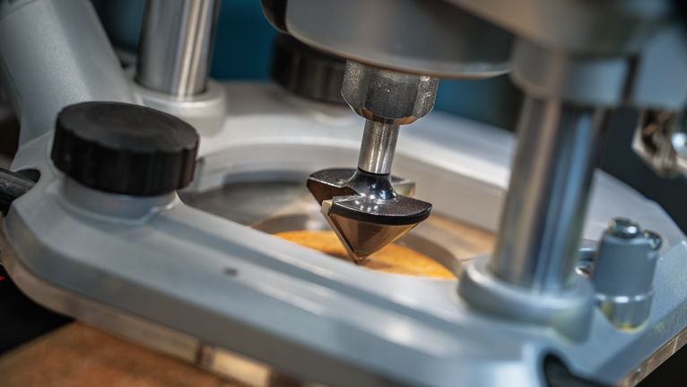 Mata router mengukir pada permukaan kayu di meja bengkel.