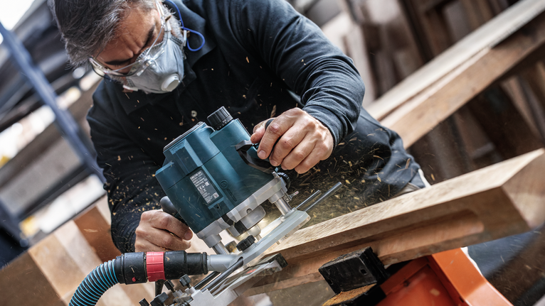Orang yang mengenakan peralatan keselamatan memotong kayu dengan router listrik.