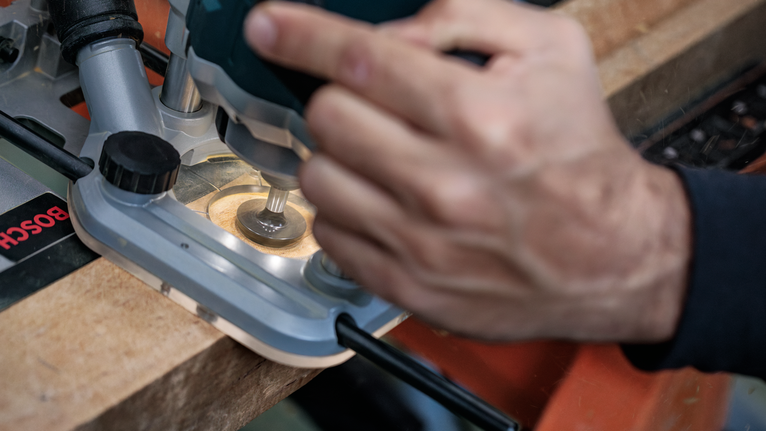 Seseorang menggunakan router untuk membentuk tepi papan kayu.