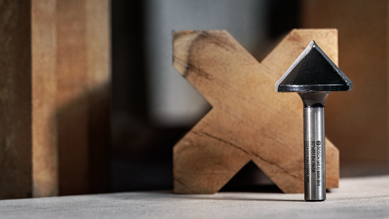 Mata router talang berdiri tegak di meja kerja di depan balok kayu.