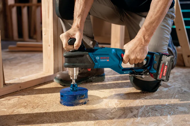 Seseorang menggunakan bor sudut tanpa kabel untuk membuat lubang besar di lantai kayu.