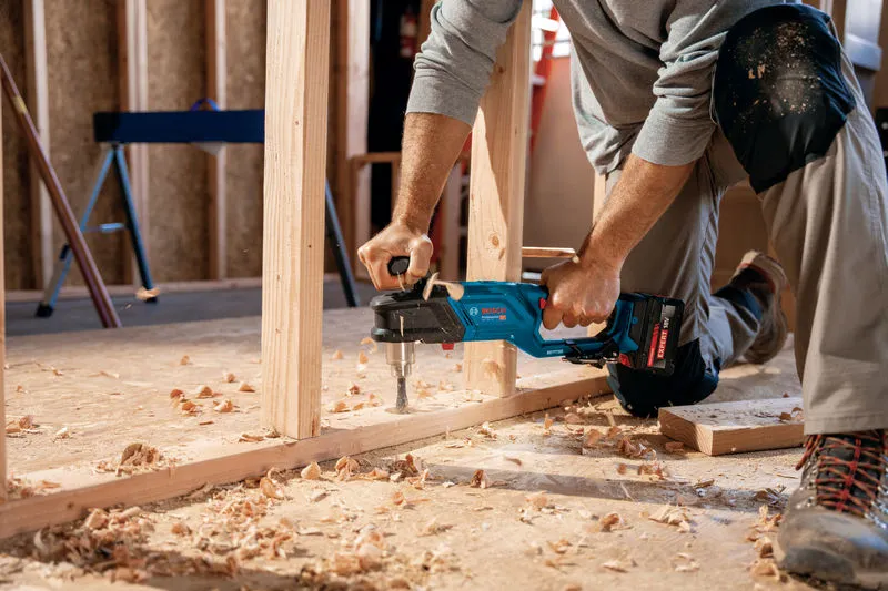 Seseorang yang mengenakan peralatan keselamatan mengebor rangka kayu dengan bor sudut tanpa kabel.