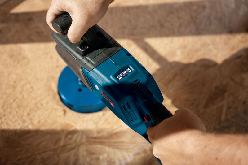 Seseorang mengoperasikan bor sudut tanpa kabel berwarna biru pada permukaan kayu.