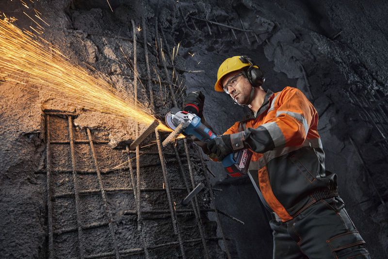 Seseorang yang mengenakan perlengkapan keselamatan menggunakan gerinda sudut untuk memotong besi beton, sehingga menimbulkan percikan api.