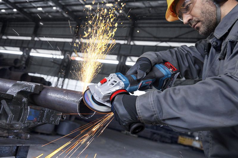 Seseorang yang mengenakan peralatan keselamatan menggerinda pipa logam dengan gerinda sudut, sehingga menimbulkan percikan api.