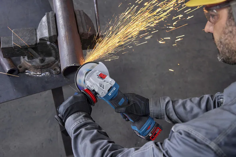 Seseorang yang mengenakan peralatan keselamatan menggunakan mesin gerinda sudut untuk memotong pipa logam.