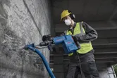 Seseorang yang mengenakan peralatan keselamatan menggunakan palu penghancur untuk memecahkan beton.