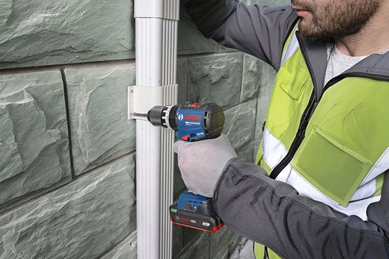 Seseorang yang mengenakan perlengkapan keselamatan menggunakan bor tanpa kabel untuk memasang braket pada dinding.