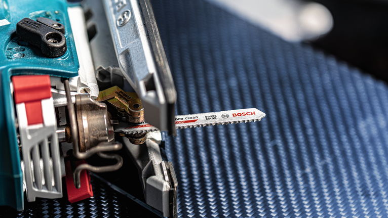 Gergaji ukir dengan bilah logam diletakkan pada permukaan biru bertekstur.