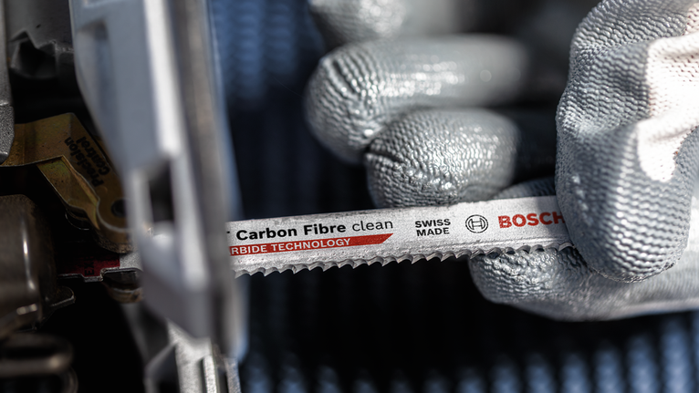 Orang yang mengenakan peralatan keselamatan memasang mata gergaji serat karbon ke dalam perkakas listrik.