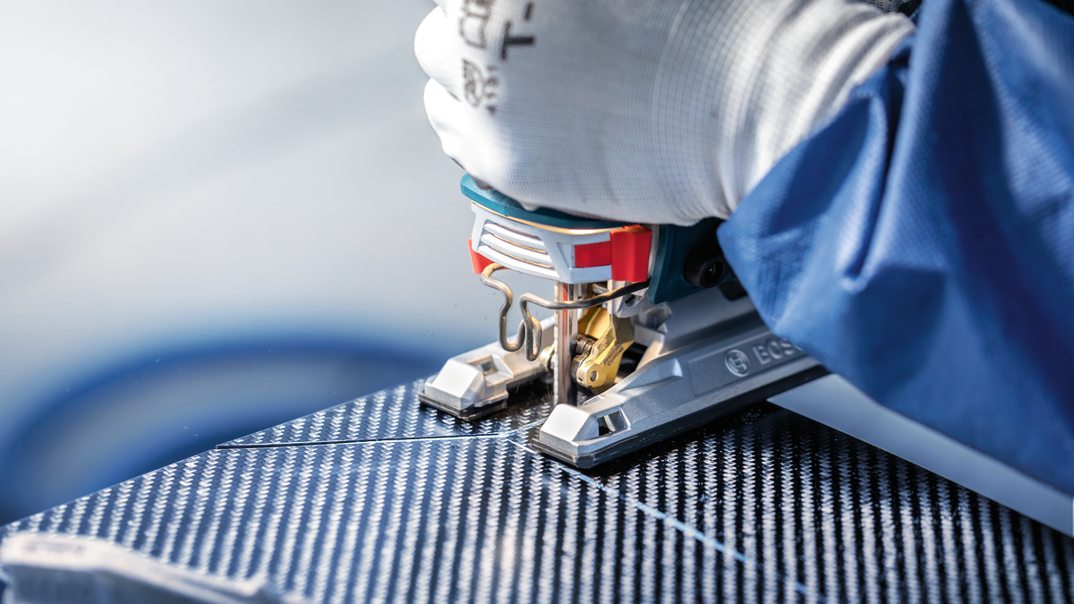 Orang yang mengenakan peralatan keselamatan memotong panel berpola dengan gergaji ukir.