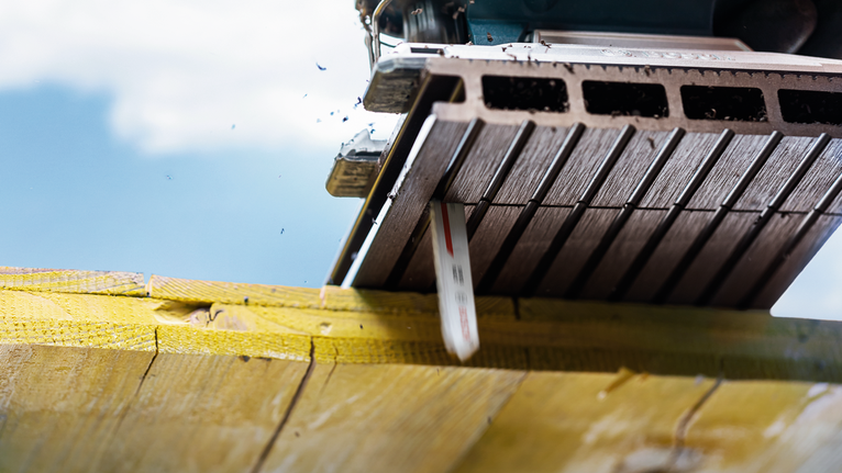 Mata gergaji memotong balok kayu di bawah cahaya luar ruangan yang terang.