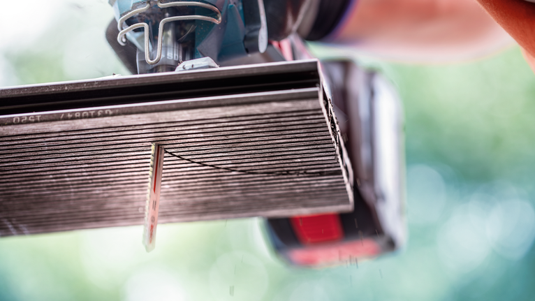 Seseorang yang mengenakan perlengkapan keselamatan menggunakan gergaji listrik untuk memotong ubin keramik.