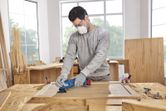 Seseorang yang mengenakan peralatan keselamatan mengampelas panel kayu dengan alat multifungsi.