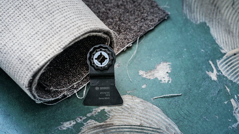 Mata pisau alat berosilasi di lantai hijau di samping karpet gulung.