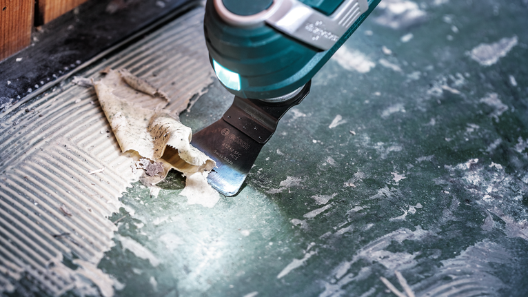 Alat berosilasi mengikis perekat dari lantai keramik.