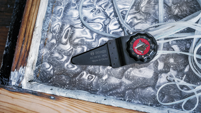 Dudukan mata pisau alat osilasi diletakkan di atas lembaran logam bertekstur di dekat bingkai kayu.