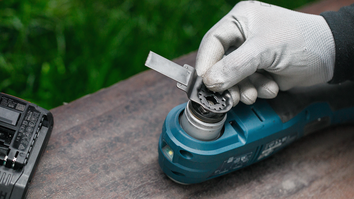 Orang yang mengenakan perlengkapan keselamatan memasang bilah pisau ke perkakas listrik berwarna biru.