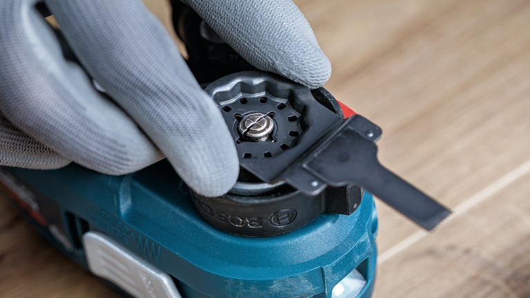 Seseorang yang mengenakan perlengkapan keselamatan sedang menyesuaikan aksesori alat pada perkakas listrik.