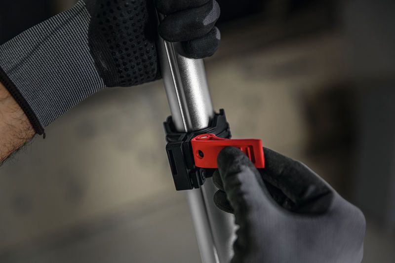 Seseorang yang mengenakan peralatan keselamatan sedang menyetel klem merah pada tiang logam.