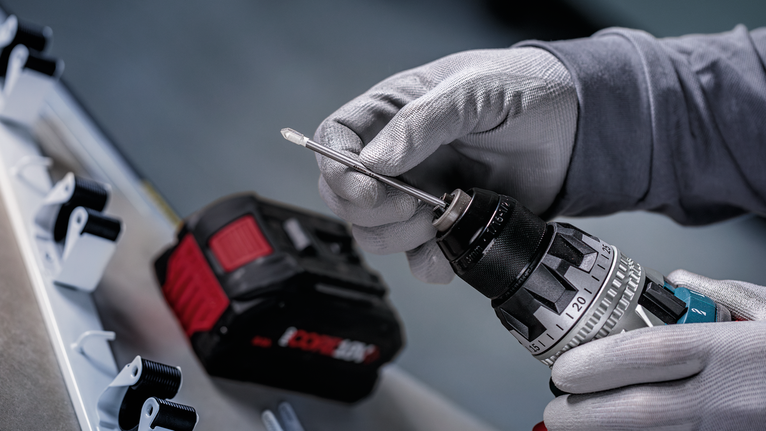 Orang yang mengenakan peralatan keselamatan memasukkan mata bor ke dalam bor tanpa kabel.