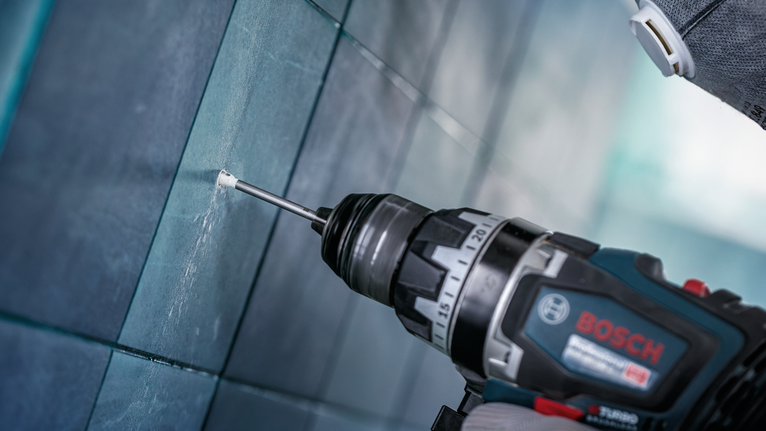 Orang yang mengenakan peralatan keselamatan mengebor lubang pada dinding ubin.