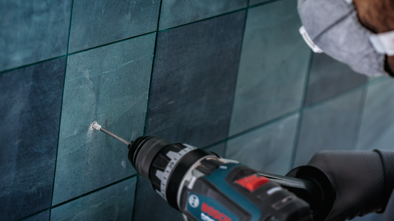 Orang yang mengenakan peralatan keselamatan mengebor lubang pada dinding ubin.