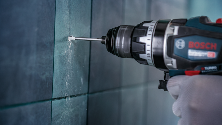 Orang yang mengenakan peralatan keselamatan mengebor dinding ubin.
