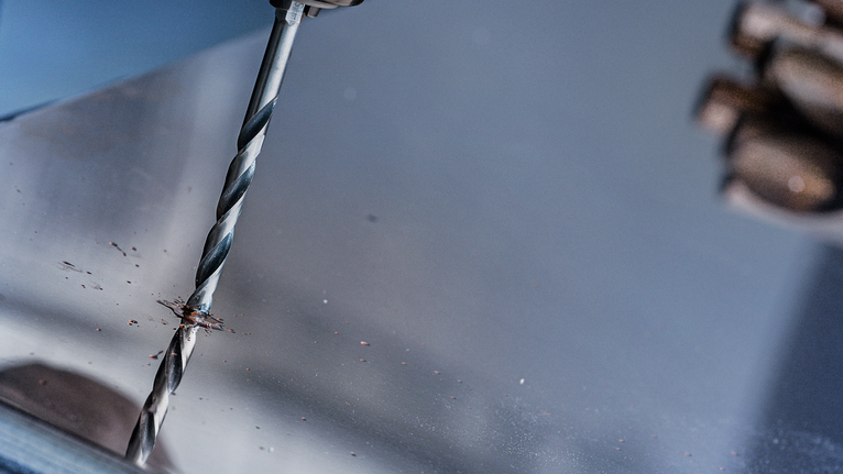 Seseorang mengebor lembaran logam.