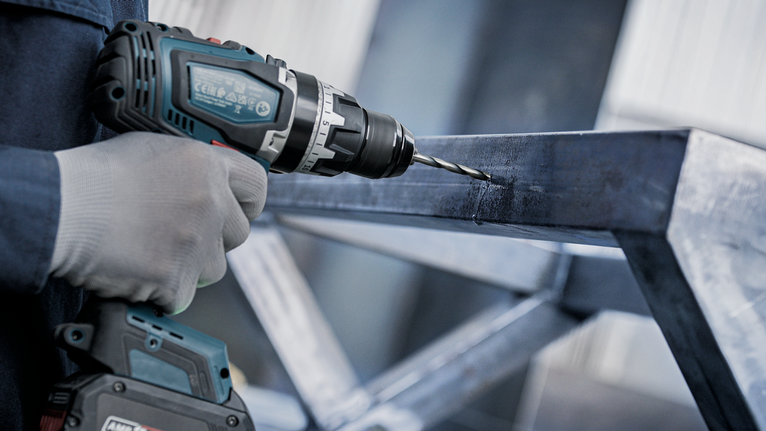 Orang yang mengenakan peralatan keselamatan mengebor balok logam.