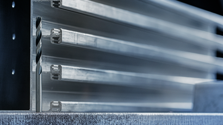 Mata bor logam diposisikan di depan profil aluminium yang ditumpuk.