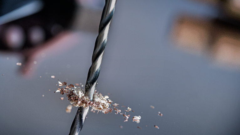 Mata bor membuat lubang pada logam dengan serutan logam yang tersebar di sekitarnya.