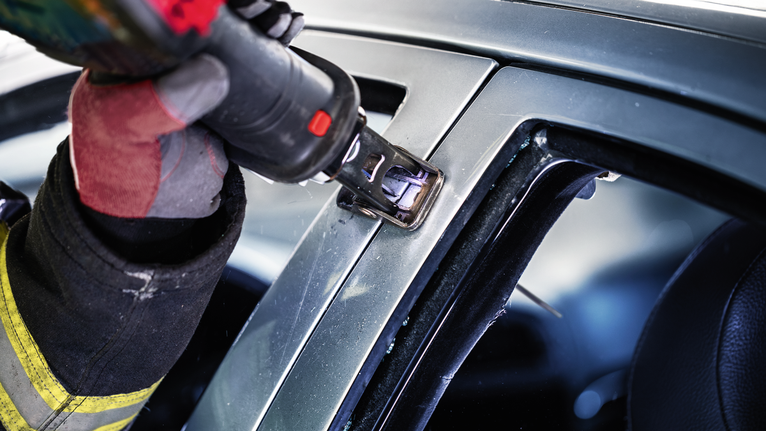 Seseorang yang mengenakan perlengkapan keselamatan menggunakan alat listrik untuk memotong rangka mobil.