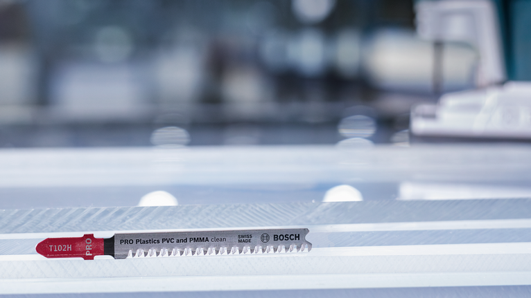 Mata pisau gergaji untuk memotong plastik diletakkan di atas permukaan kerja yang bergaris.