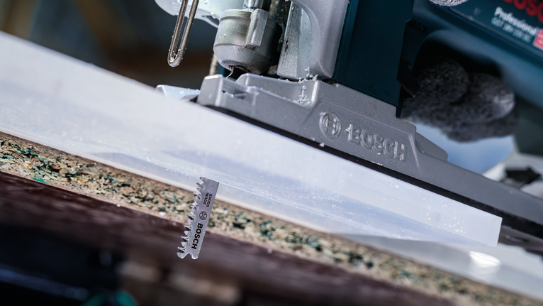 Seseorang yang mengenakan peralatan keselamatan mengoperasikan gergaji mesin untuk memotong papan laminasi.