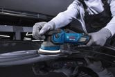 Seseorang yang mengenakan perlengkapan keselamatan memoles permukaan mobil dengan mesin pemoles tanpa kabel.