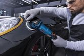 Seseorang yang mengenakan perlengkapan keselamatan menggunakan alat pemoles pada spatbor mobil.
