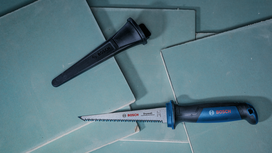 Gergaji tangan dan penutup mata pisau diletakkan di atas tumpukan lembaran drywall.