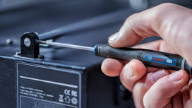 Seseorang menggunakan obeng untuk mengencangkan sekrup pada peralatan elektronik.