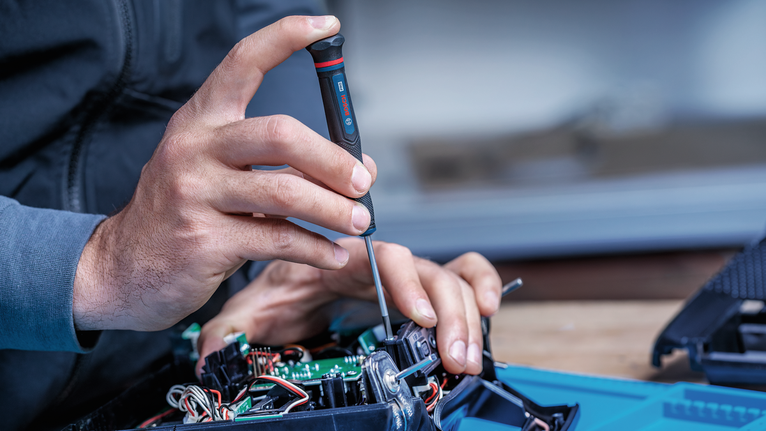 Seseorang menggunakan obeng untuk memperbaiki perangkat elektronik.