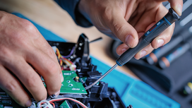 Seseorang menggunakan obeng untuk mengerjakan komponen elektronik.