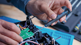 Seseorang menggunakan obeng presisi untuk merakit papan sirkuit elektronik.