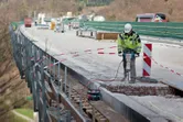 Seseorang yang mengenakan peralatan keselamatan mengoperasikan pemecah gelombang untuk menghancurkan beton di sebuah jembatan.