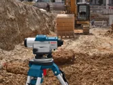 Alat perataan laser pada tripod di lokasi konstruksi dekat ekskavator.